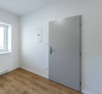 Interiér pokoje s bílými stěnami, podlahou s dřevěným dekorem a oknem.