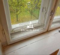 Pohled z okna v rodinném domě s výhledem na podzimní zahradu a stromem.