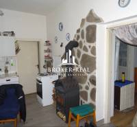 Kuchyně v rodinném domě se sporákem, pecí a kamenným obkladem u stěny.