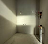 Prázdná místnost s betonovou podlahou a instalacemi v rodinném domě.