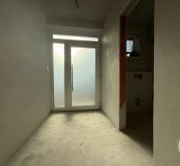 Interiér rodinného domu s bílými stěnami a prosklenými dveřmi na konci chodby.