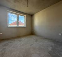 Pokoj v rodinném domě, stěny bez dekorací, vidět střechu sousední budovy.