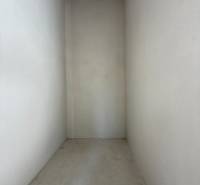 Úzký, prázdný interiér rodinného domu s betonovou podlahou a bílými stěnami.