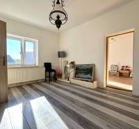 Pokoj v rodinném domě s bílými stěnami, podlahou s dřevěným dekorem a velkým oknem.