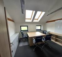 Kancelář s podlahou s dřevěným dekorem, střešními okny a stoly se židlemi.