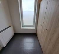 Kancelář s dlažbou, úložným prostorem a velkým oknem, bez nábytku.