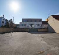 Pozemek v Nových Zámcích vhodný k bydlení, obklopený budovami, čisté asfaltové plochy.