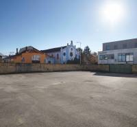 Fotografie pozemku k bydlení v Nových Zámcích. Záběr ukazuje budovy v pozadí.