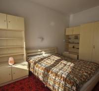 Ložnice v rodinném domě se světlým nábytkem a vzorovaným přehozem na postel.