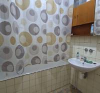 Koupelna v rodinném domě, vana se závěsem, umyvadlo s mýdlem a zrcadlo.