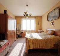 Ložnice v rodinném domě s nábytkem, lustrem a obrazem na stěně.