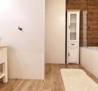 Koupelna s bílými obklady a podlahou s dřevěným dekorem v 3-pokojovém bytě.