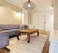 Obývací pokoj v 3-pokojovém bytě s pohovkou, dřevěným stolem a podlahou s dřevěným dekorem.