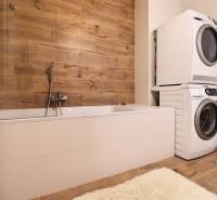 Koupelna s vanou, pračkou, sušičkou a stěnou s dřevěným dekorem ve 3-pokojovém bytě.