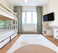 Pokoj ve 3-pokojovém bytě s patrovou postelí, televizí a podlahou s dřevěným dekorem.