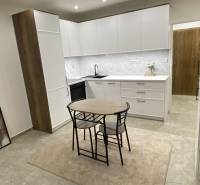 Kuchyně v 1-pokojovém bytě s bílými skříňkami a jídelním stolem.