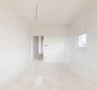 Prostorná světlá místnost v rodinném domě s bílými stěnami a menším oknem.