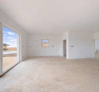 Interiér rodinného domu s velkými okny a světlými stěnami, podlaha s dřevěným dekorem.