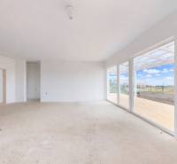 Bílý obývací pokoj v rodinném domě s velkými okny a výhledem do zahrady.