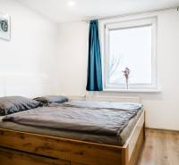 Ložnice s podlahou s dřevěným dekorem a postelí v dvoupokojovém bytě, modrý závěs na okně.