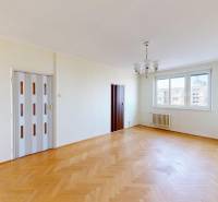 Obývací pokoj v 3-pokojovém bytě s velkými okny a podlahou s dřevěným dekorem.