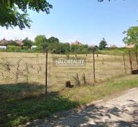 Rovinatý pozemek ohraničený plotem v Zahradách Marcelové, v pozadí je vidět domy.