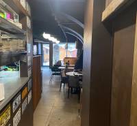 Interiér gastro prostorů s talíři na polici, tabule, stoly a židle.