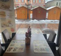 Zimní scenérie přes okno gastro prostoru s pohledem na dřevěné stolky.