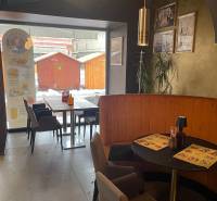 Gastro prostory s kavárenským sezením, dekoracemi na stěnách a výhledem na dřevěné stánky venku.