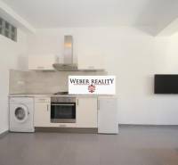 Kuchyně v 2-pokojovém bytě s bílou linkou, pračkou a televizí na stěně.