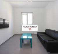 Obývací pokoj dvoupokojového bytu s černou sedačkou, televizorem na stěně a nízkým stolkem.