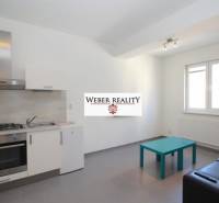 Kuchyně v 2-pokojovém bytě s šedou podlahou, kuchyňskou linkou a posezením.