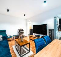 Obývací pokoj dvoupokojového bytu s podlahou s dřevěným dekorem a modrými sedacími soupravami.