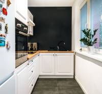 Kuchyně v 2-pokojovém bytě s černou stěnou, dřevěným dekorem a bílými skříňkami.
