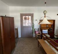 Interiér rodinného domu s nábytkem a kobercem, středová lampa a police s nápoji.