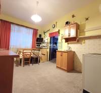 Kuchyně v rodinném domě s dřevěným dekorem, světlé stěny, stůl se židlemi.