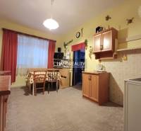 Kuchyně v rodinném domě s dřevěným dekorem, jídelním stolem a skříňkami.