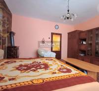 Interiér rodinného domu s dřevěným nábytkem, kobercem a postelí s barevným přehozem.