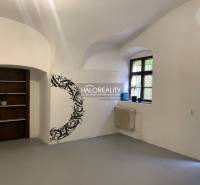 Interiér kanceláře s bílými stěnami, oknem, nástěnnou dekorací a dřevěným regálem.