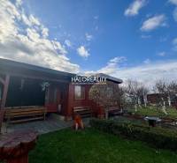 Dřevěná chatka v zahradách Spišské Nové Vsi s lavičkami a květinovým záhonem.