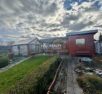 Dřevěná chata v zahradách ve Spišské Nové Vsi, obklopená upraveným trávníkem a keři.