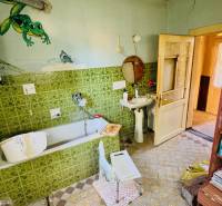 Koupelna rodinného domu s vanou, zelenými obklady a poličkou s kosmetikou.
