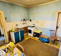 Kuchyně v rodinném domě s modrými stěnami, starším nábytkem a praktickým vybavením.