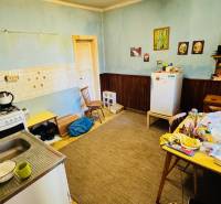 Kuchyně v rodinném domě s jídelním stolem, starším sporákem a ledničkou.