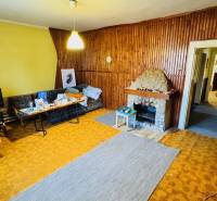 Obývací pokoj v rodinném domě s krbem a dřevěným obkladem stěn.