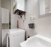 Koupelna 3pokojového bytu se spotřebiči, umyvadlem a zrcadlem na stěně.