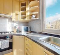 Kuchyně v 3-pokojovém bytě s dřevěnými skříňkami, plynovým sporákem a výhledem z okna.