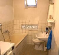 Koupelna se starší vanou, umyvadlem a pračkou v rodinném domě.