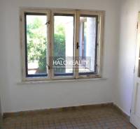 Pokoj v rodinném domě s dlaždicovou podlahou a okny směřujícími do zeleně.