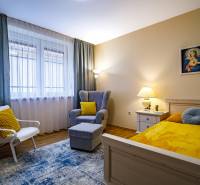 Pokoj v rodinném domě s postelí, křeslem, stolkem a podlahou s dřevěným dekorem.